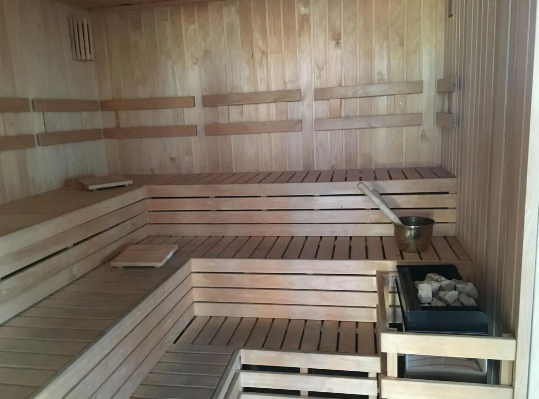 Un sauna avec des bancs en bois et un seau en métal.