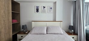 Un lit bien fait, avec une tĂȘte de lit, des tables de chevet avec des lampes, une armoire en bois et des Ćuvres dâart accrochĂ©es au mur.
