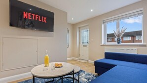 Un salon avec une télévision, un canapé, une table à manger avec une bouteille et une assiette, et une fenêtre donnant sur des maisons.