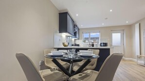Une cuisine moderne avec un coin repas, comprenant une table et des chaises en verre, une hotte noire et une vue sur la ville grâce à de grandes fenêtres.