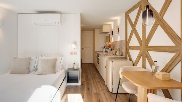 Moderni hotellihuone, jossa on sänky, yöpöytä ja pieni keittokomero.