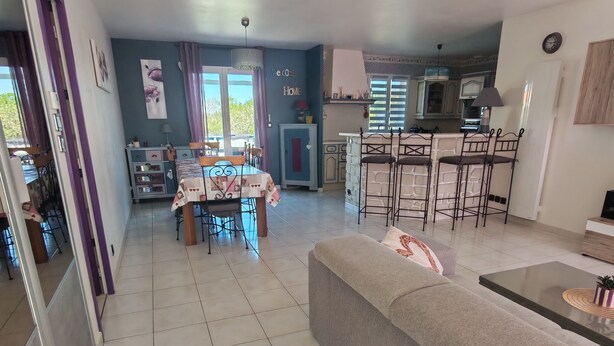 Ampla sala de estar com sofá, mesa de jantar e cozinha ao fundo.