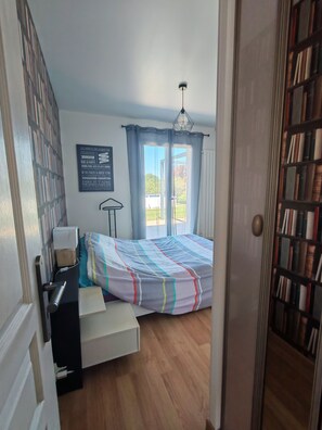Ein Schlafzimmer mit Bett, Schreibtisch, Bücherregal, einem Fenster mit Vorhängen und einer Tür.