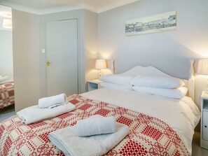 A hotel room with a bed, two bedside tables, a door, and a painting on the wall. - Brewery Cottage (Saundersfoot)