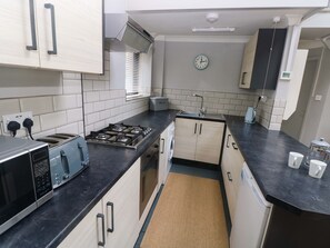 A modern kitchen with a gas stove, toaster, microwave, and a clock on the wall. - Brewery Cottage (Saundersfoot)