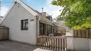 A cottage with a stone wall, a wooden deck, and a small outdoor seating area. - Brewery Cottage (Saundersfoot)