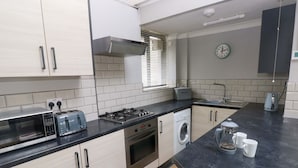 A modern kitchen with a microwave, toaster, stove, oven, and washing machine. - Brewery Cottage (Saundersfoot)