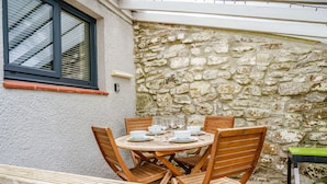A stone wall, wooden table, and chairs in a covered outdoor area. - Brewery Cottage (Saundersfoot)