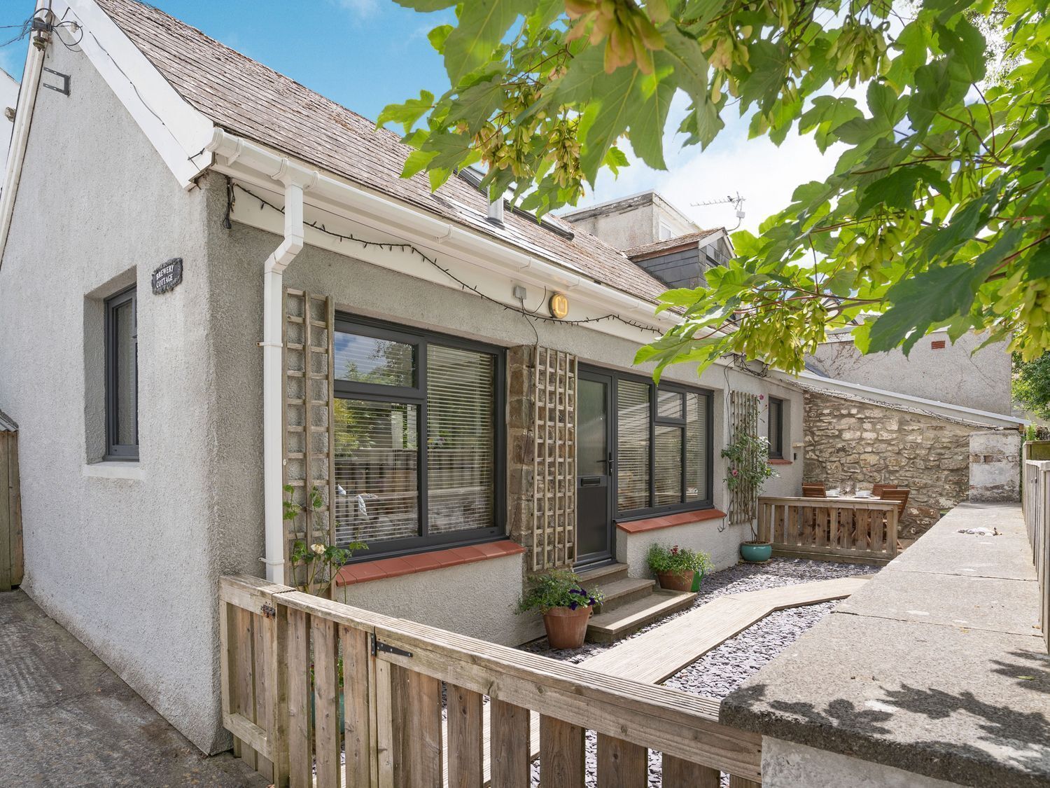 A cottage with a stone facade, large windows, and a wooden deck with potted plants.