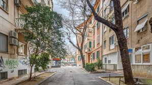 Una tranquilla strada cittadina fiancheggiata da edifici a più piani, alcuni con balconi e condizionatori.