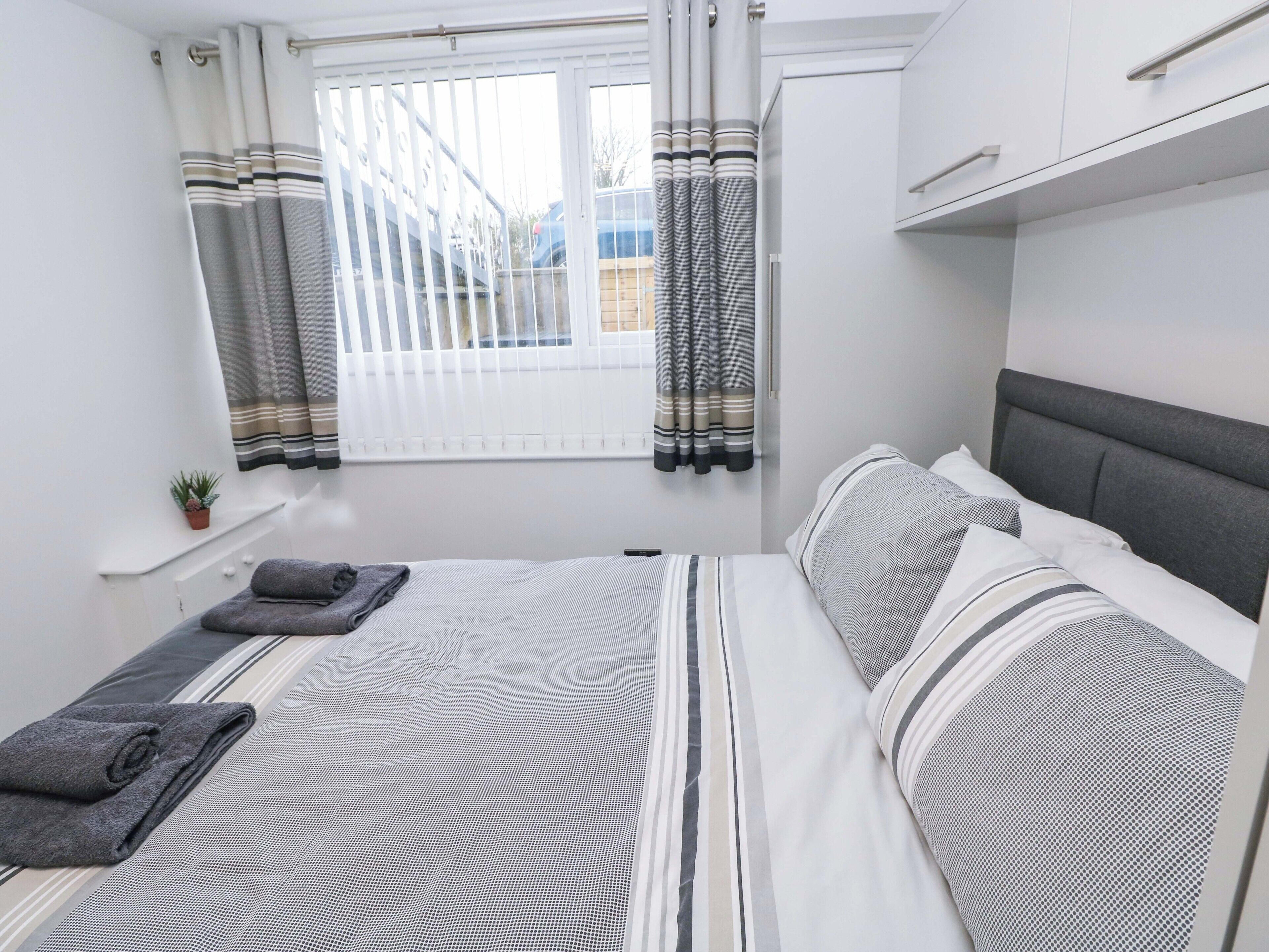 A bedroom with a bed, pillows, a window with curtains, a radiator, and a small plant.