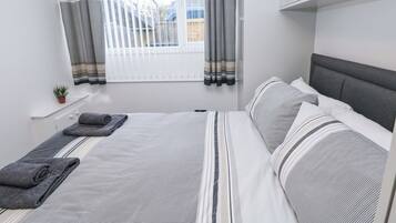 A bedroom with a bed, pillows, a window with curtains, a radiator, and a small plant.