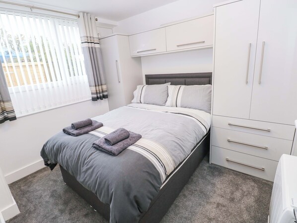 A bedroom with a bed, a wardrobe, and a window with curtains. - 3 Devon Court (Pembroke)