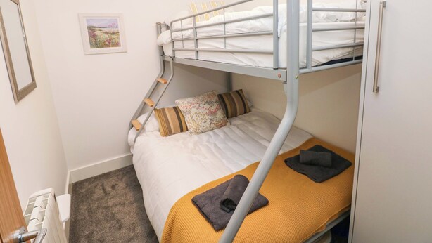 Un letto a castello con un posto inferiore, un letto singolo con coperta gialla, un cuscino e un piccolo tappeto.