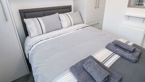 Un lit bien fait, avec une literie à rayures, une tête de lit grise et une serviette grise posée sur le côté.