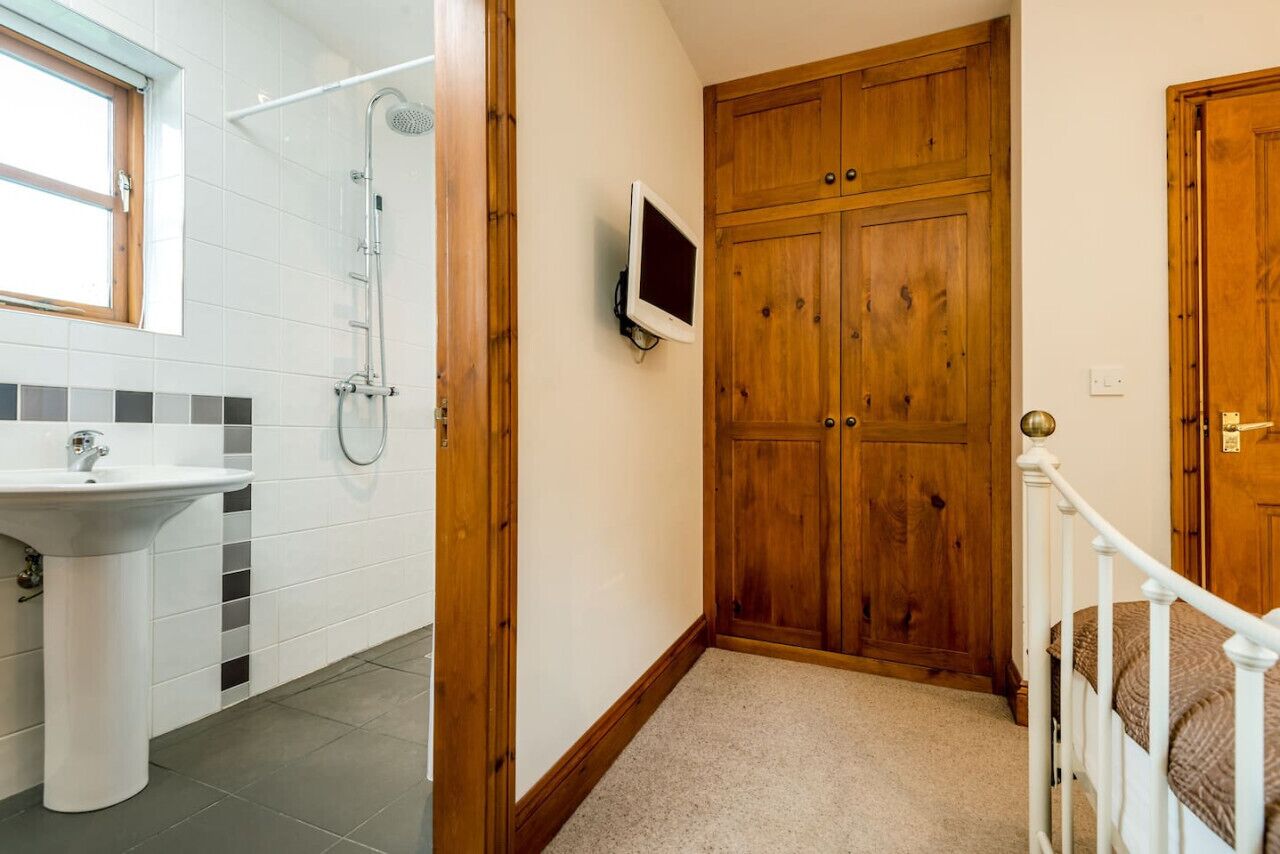 A bathroom with a sink, shower, and wooden wardrobe.