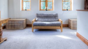 A room with a sloped ceiling, wooden beams, a bench, and two windows with a view of trees.