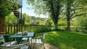 Een terras met een tafel en stoelen, een spiraaltrap en uitzicht op een groen landschap met een houten omheining.