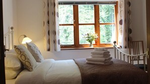 A hotel room with a bed, a lamp, a window with curtains, a chair, and a vase with flowers.
