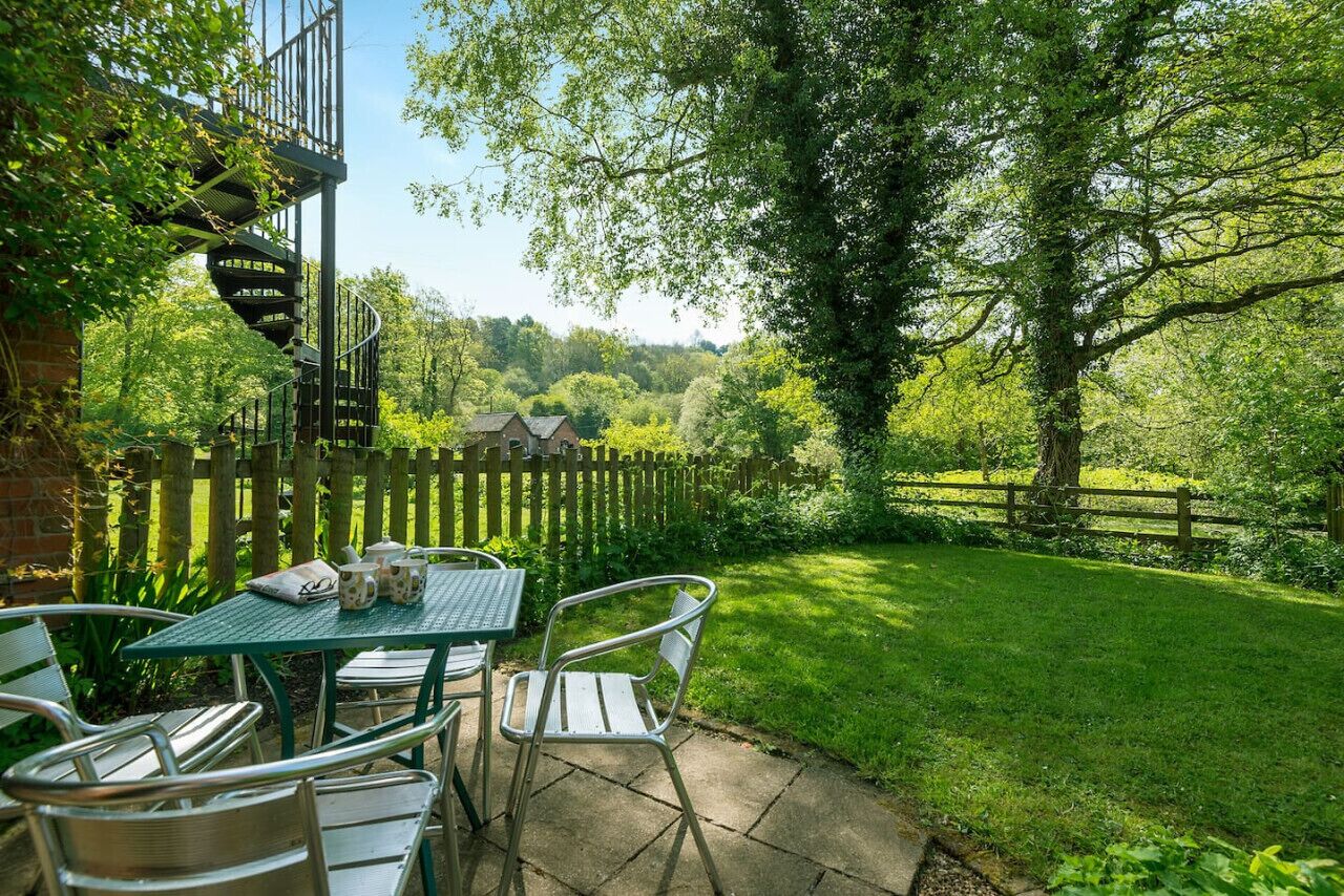 Een terras met een tafel en stoelen, een spiraaltrap en uitzicht op een groen landschap met een houten omheining.