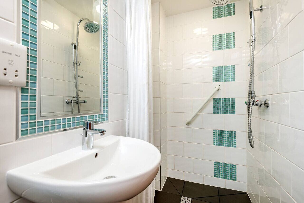 Un bagno con lavandino, specchio, doccia e pareti piastrellate.