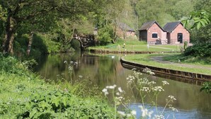 A tranquil riverside scene with a bridge, a small brick building, and lush greenery.