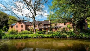 A traditional brick building with a reflective pond, surrounded by lush greenery and trees.