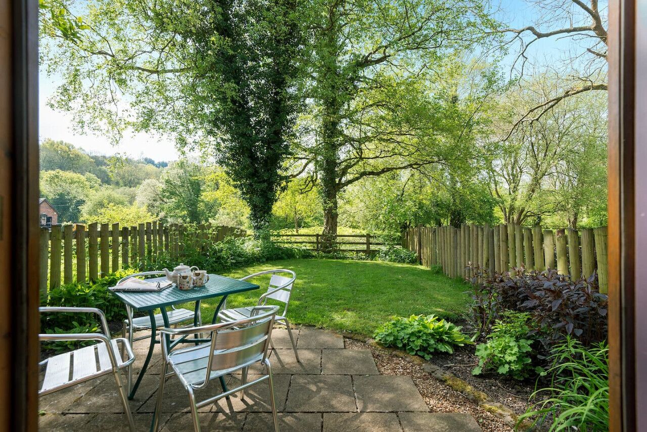 Een terras buiten, met een tafel en stoelen, omringd door een houten hek en groen.