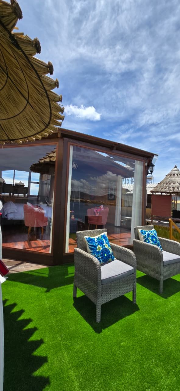 A glass-enclosed outdoor seating area with wicker chairs and a thatched roof structure.