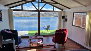 A room with a large window overlooking a lake, a red chair, a blue chair, and a small table with a plant. - Uros Kaivalia Lodge (Puno)