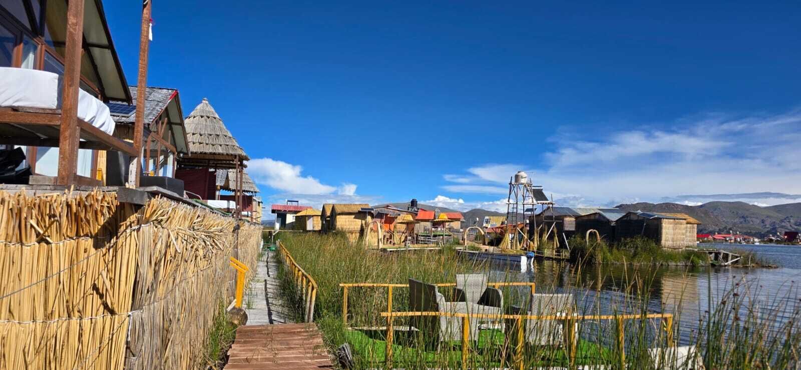 Una edificación de madera tradicional con techo de paja, una escalera de madera que conduce a un muelle, y un cuerpo de agua con barcos.