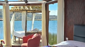 A bedroom with a large bed, a view of the sea, a wooden ceiling, and a glass door leading to a balcony. - Uros Kaivalia Lodge (Puno)