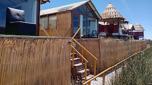 A building with large windows, a staircase, and a thatched-roof structure. - Uros Kaivalia Lodge (Puno)