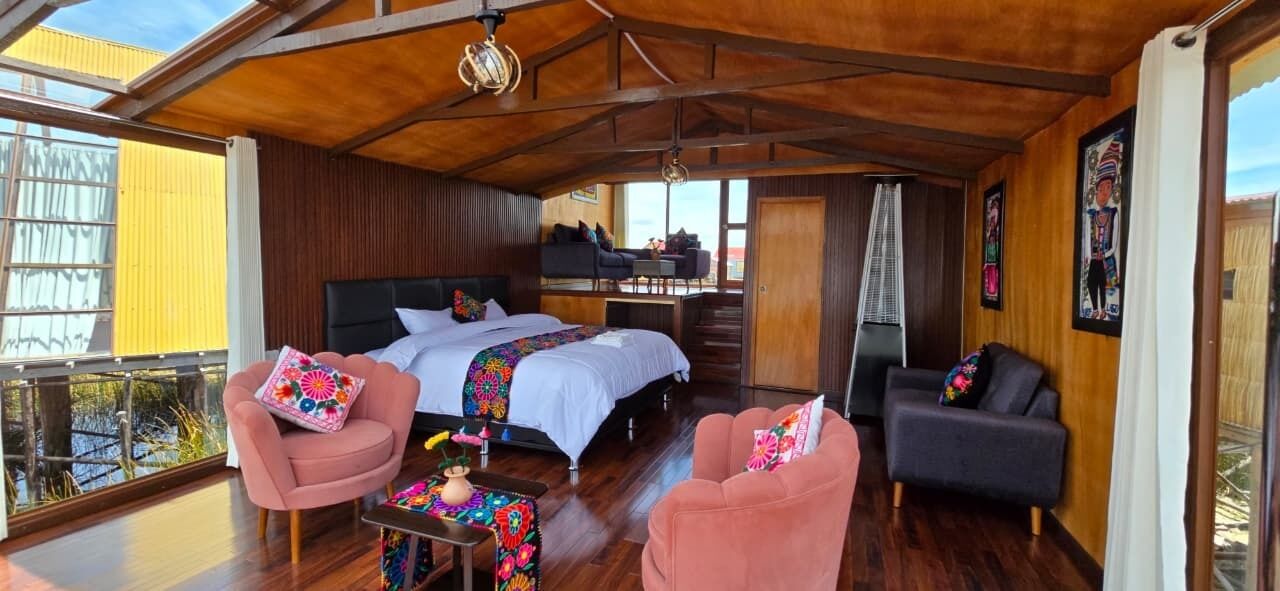 Ein Zimmer mit einem Bett, zwei rosafarbenen Stühlen, einem kleinen Tisch und einem dunklen Sofa.
