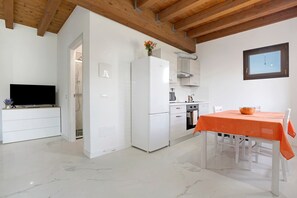 A modern kitchen with white appliances, a dining table with an orange tablecloth, and a TV on a white cabinet. - Apartment 'Alessia' with Shared Pool, Garden, and Wi-Fi (Jesolo)