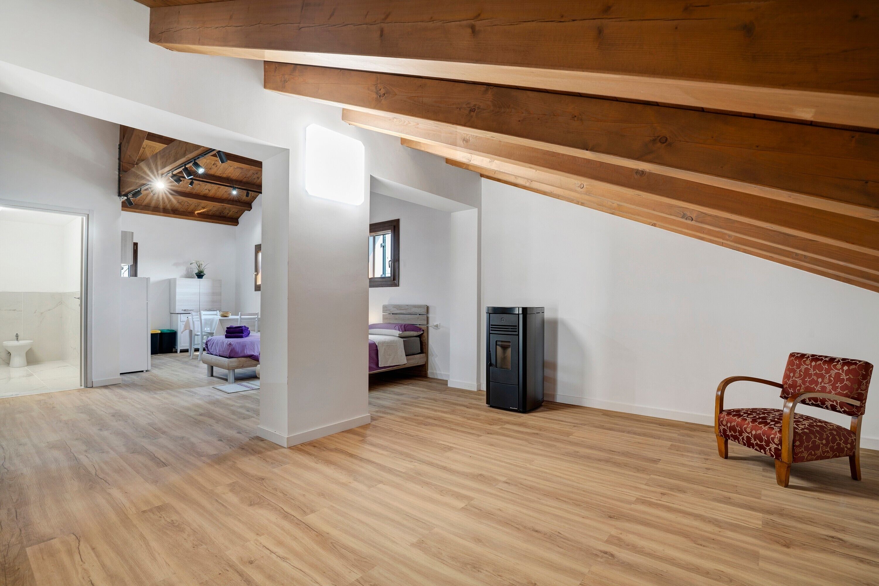 Ein geräumiges Schlafzimmer im Loft-Stil mit schrägverdeckter Decke, einem Bett, einem Sessel und einem Kühlschrank.