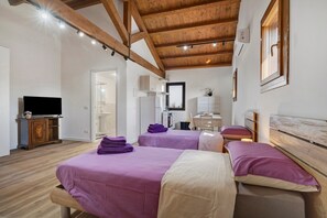 Ein Schlafzimmer mit zwei Betten, Holzbalken, einem Fernseher und einem im Hintergrund sichtbaren Badezimmer.