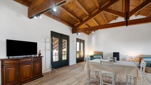 A spacious room with a wooden ceiling, a dining table with chairs, a television on a cabinet, and a door leading to an outdoor area. - Apartment 'Marina' with Shared Pool, Garden, and Wi-Fi (Jesolo)