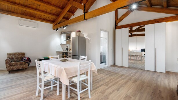 A spacious room with a high wooden ceiling, a dining table with chairs, a sofa, and a kitchen area with a refrigerator and cabinets. - Apartment 'Marina' with Shared Pool, Garden, and Wi-Fi (Jesolo)