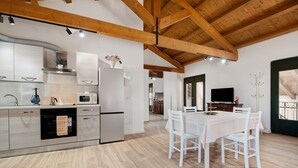 A modern kitchen with wooden beams, stainless steel appliances, and a dining area with white furniture. - Apartment 'Marina' with Shared Pool, Garden, and Wi-Fi (Jesolo)