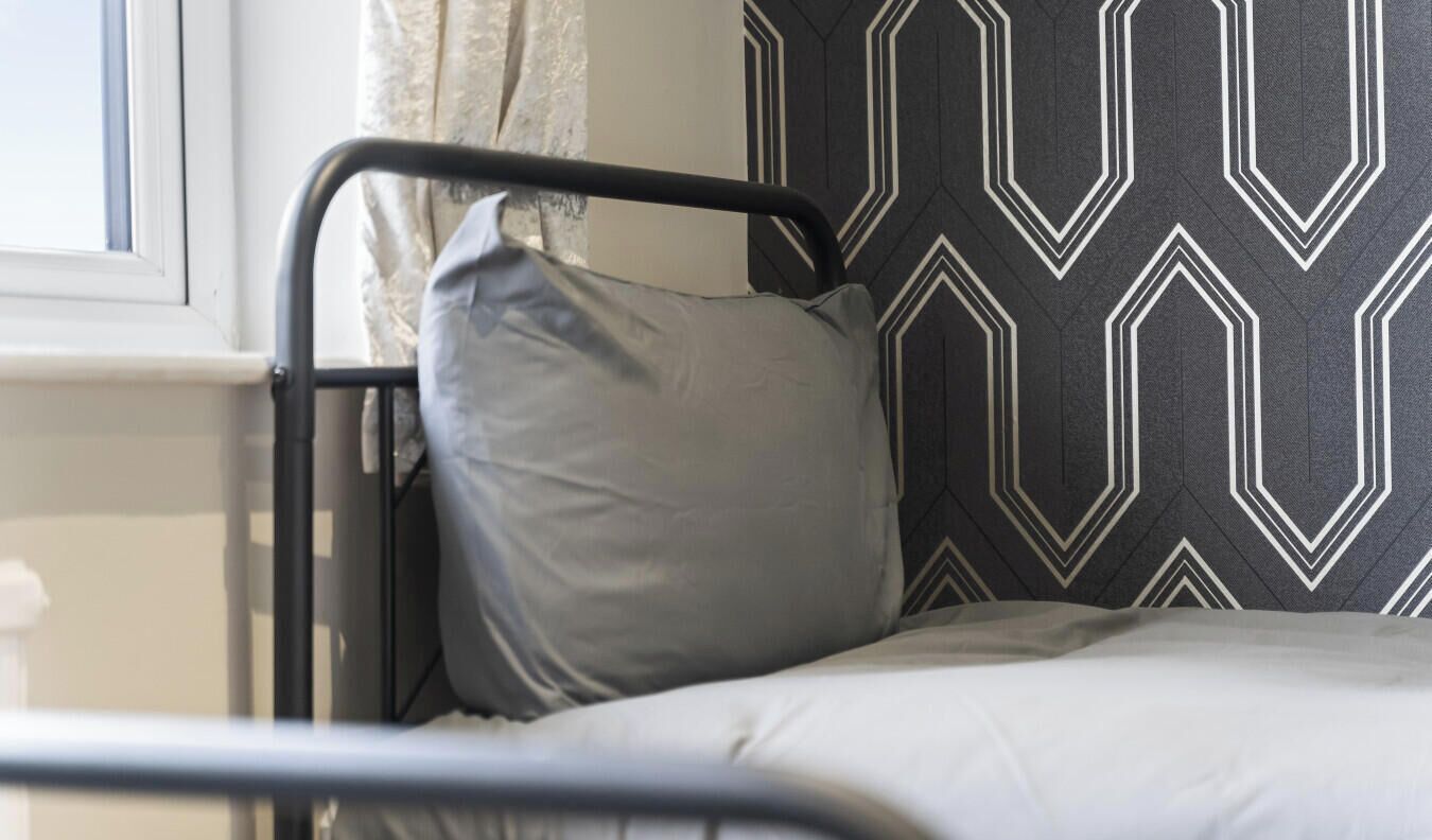 A bed with a metal frame, a grey pillow, and a patterned wall.