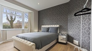 Quarto com cama, mesa de cabeceira e janela com vista para árvores.