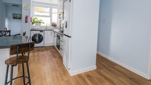 A modern kitchen with white cabinets, a washing machine, and a dining area with a bar stool. - Clifftop House (Bournemouth)