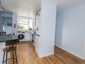 A modern kitchen with white cabinets, a washing machine, and a dining area with a bar stool. - Clifftop House (Bournemouth)