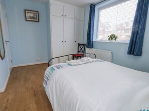 A bedroom with a bed, a chair, a wardrobe, a radiator, and a window with curtains. - Clifftop House (Bournemouth)