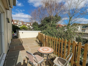 A patio with two wicker chairs and a mosaic table, surrounded by a wooden fence and a view of neighboring houses.