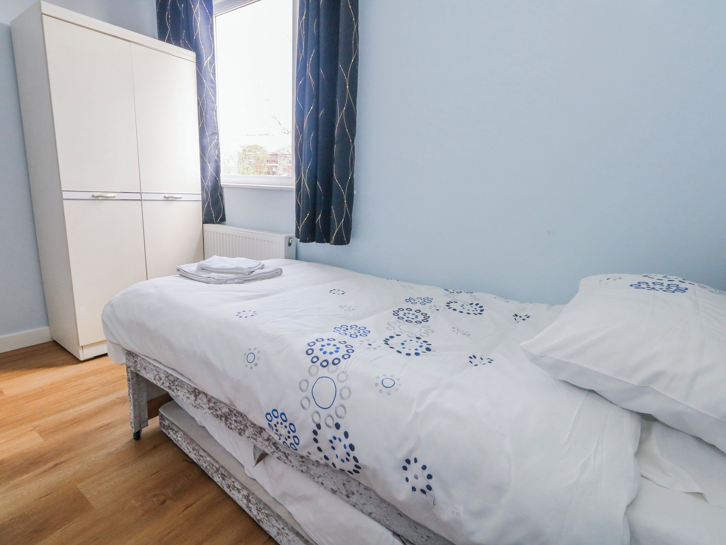 Un dormitorio con cama, armario y ventana con cortinas.