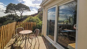 A patio with a table and chairs, a wooden fence, and a large sliding glass door. - Clifftop House (Bournemouth)