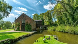 A brick building with a pond, ducks, and greenery. - Wharf Cottage: Swimming lake, BBQ Hut, Games Room (Alton Towers & Staffordshire Villages)