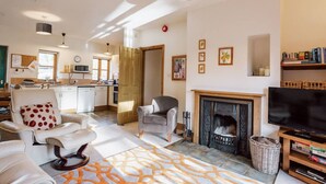 A spacious living room with a fireplace, a television, and a kitchen in the background. - Clinkum Cottage Swimming Lake, BBQ hut, Games Room (Alton Towers & Staffordshire Villages)